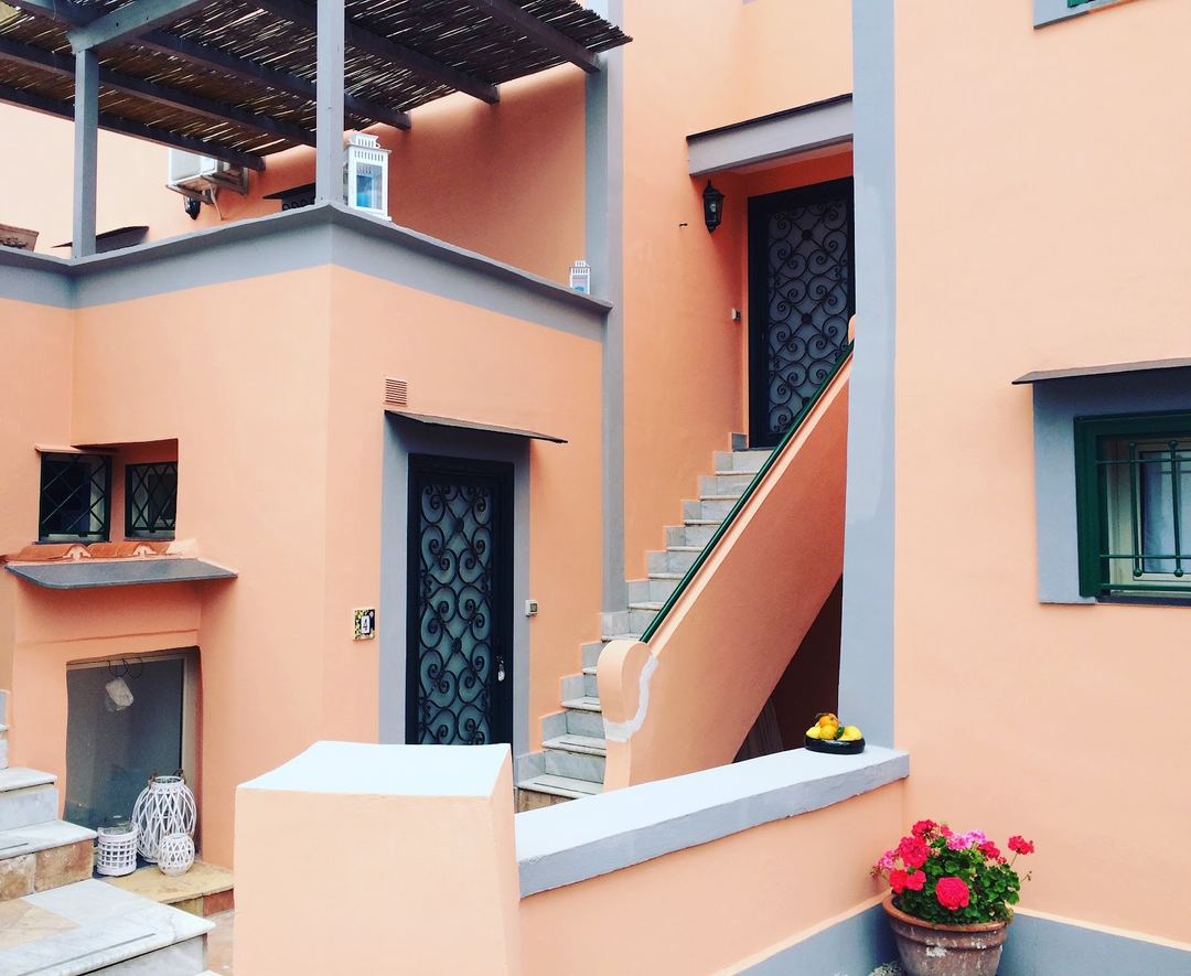 Charming terracotta-colored exterior of Il Borghetto featuring ornate black doors, gray trim accents, and a potted flowering plant on the entrance level.