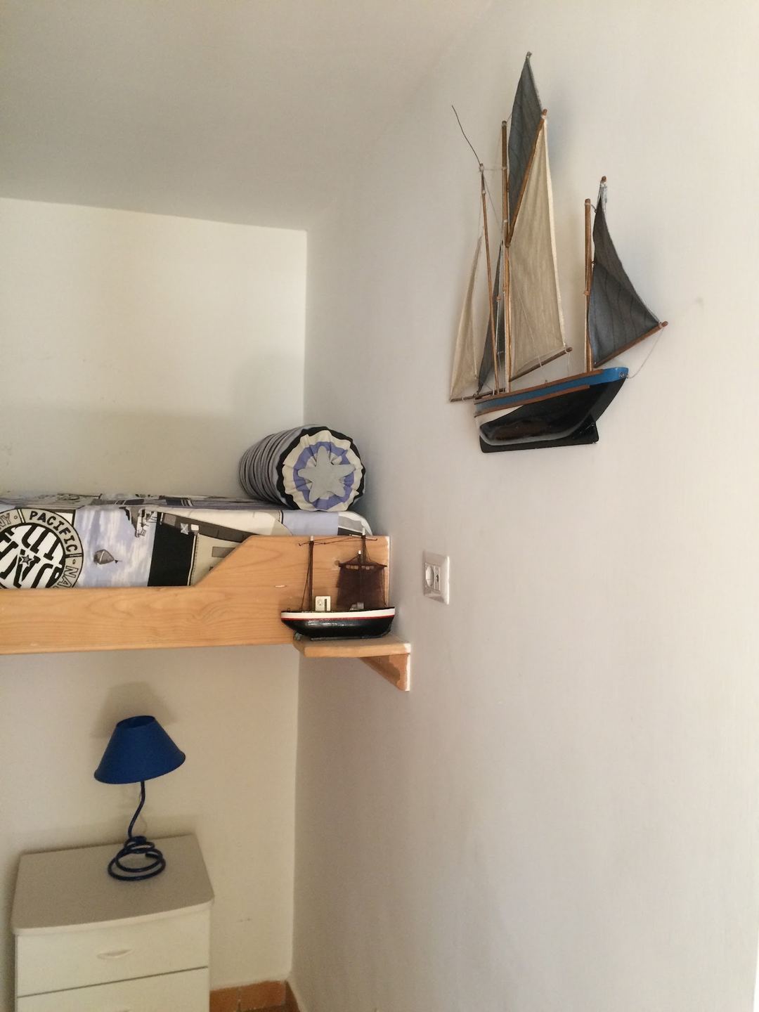 A nautical-themed room corner featuring decorative wooden sailing ship models mounted on the wall above a wooden shelf.