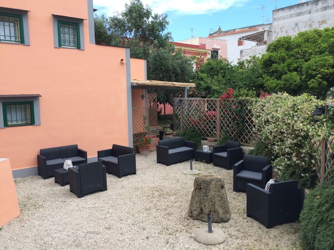 A charming courtyard seating area with black wicker furniture arranged on gravel, surrounded by a salmon-pink building and lush climbing ivy.